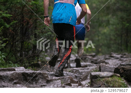 Rear view athlete running muddy stones trail during marathon in heavy rain Rear view athlete running muddy stones trail during marathon in heavy rain 129579027