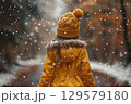 Happy girl in a yellow raincoat walks in the rain 129579180