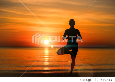 Silhouette of person in tree yoga pose on beach against beautiful orange sunset over ocean, concept for balance and harmony 129579233