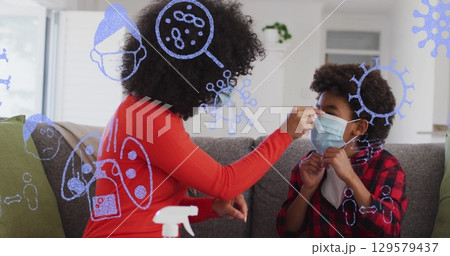 Image of pandemic icons over african american mother and son in face masks sitting on sofa 129579437