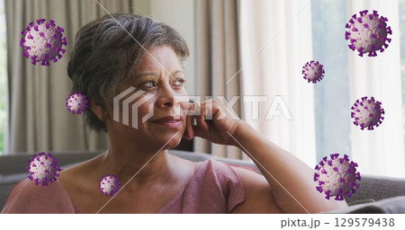 Image of coronavirus cells rotating over thoughtful senior woman with short hair sitting on sofa 129579438