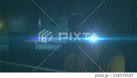 Image of blue light spot moving over african american woman wearing vr headset at home 129579587