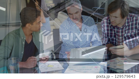Three colleagues reviewing design sketches in office meeting room, with laptop, tablets, smartphone 129579643