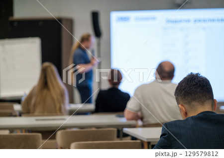 Audience attending a business seminar with a speaker presenting in the background 129579812