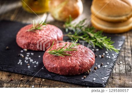 Raw burger beef patties on cutting board on wooden table. 129580057