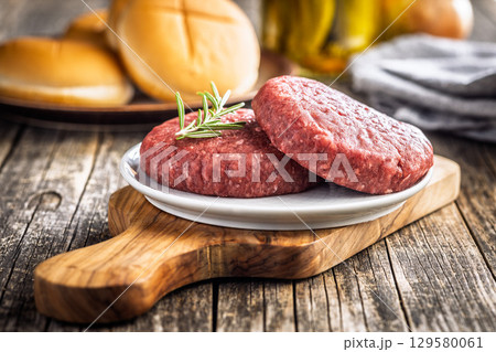 Raw burger beef patties on plate on wooden table. 129580061