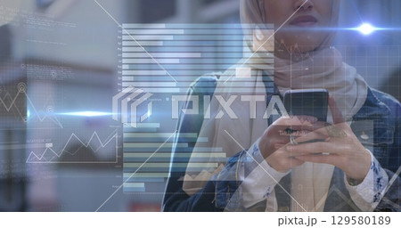 Image of flared lights with graphs over midsection of woman in scarf using smartphone 129580189