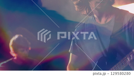 Playing guitarist strumming strapped electric guitar onstage with haze and stage lights, copy space Playing guitarist strumming strapped electric guitar onstage with haze and stage lights, copy space 129580280