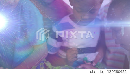 Image of light trails over diverse schoolchildren holding plants 129580422