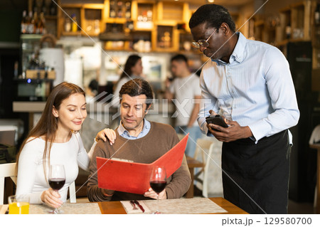 African waiter tells restaurant customers about the range of dishes and wines African waiter tells restaurant customers about the range of dishes and wines 129580700