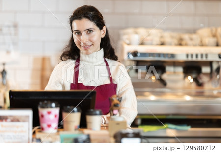 Woman cashier stands behind the counter in a coffee shop 129580712