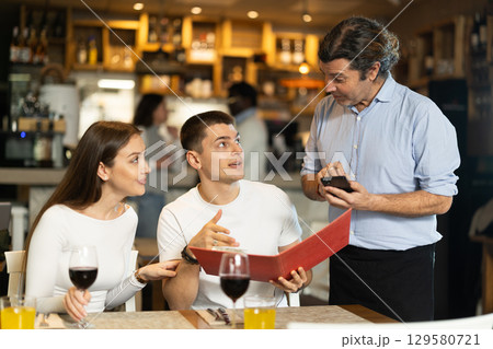 Couple chooses food from the menu and asks the waiter Couple chooses food from the menu and asks the waiter 129580721