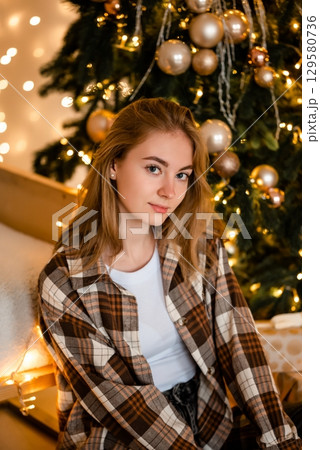Woman Relaxing by Christmas Tree with Festive Decor Woman Relaxing by Christmas Tree with Festive Decor 129580736