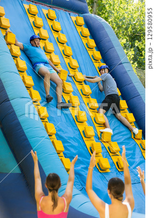 Cheerful man sliding down inflatable slide in outdoor amusement park 129580955