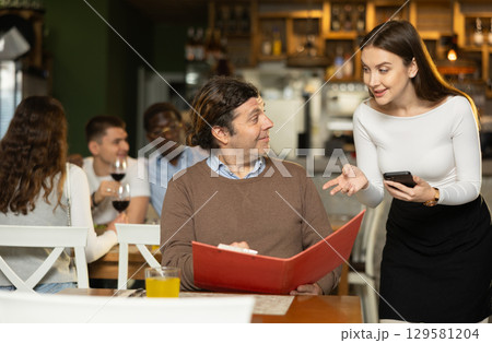 Girl waiter communicates with male customer, answers questions about composition of dish of day 129581204