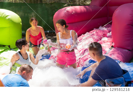 Cheerful men and women playing in foam pool in amusement park 129581218