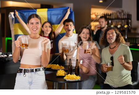Company of sports fans waving flag of Sweden and supporting national team with beer in bar 129581570