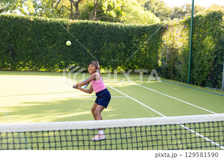 Hispanic girl wearing pink sportswear with racket focusing on yellow ball over net on tennis court Hispanic girl wearing pink sportswear with racket focusing on yellow ball over net on tennis court 129581590