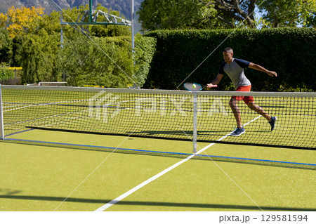 Male tennis player lunging with racket, hitting yellow ball above net on grass court, copy space 129581594
