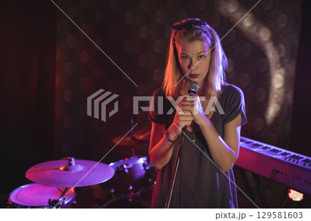 Female vocalist performing on small stage under colored spotlights with microphone and drum kit Female vocalist performing on small stage under colored spotlights with microphone and drum kit 129581603