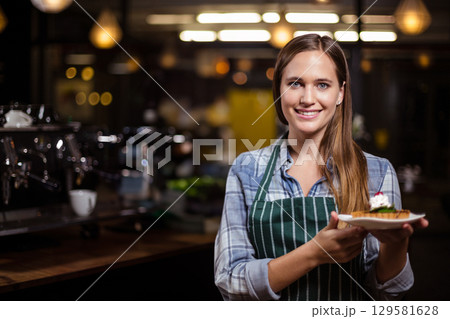 Woman wearing green apron presenting dessert plate with strawberry cream at coffee shop, copy space Woman wearing green apron presenting dessert plate with strawberry cream at coffee shop, copy space 129581628