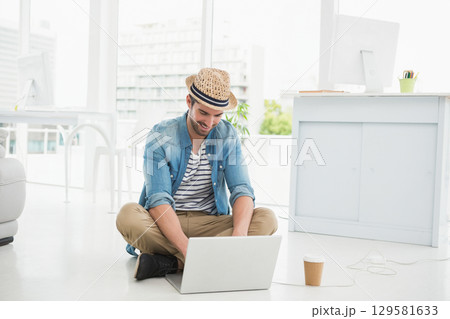 Male wearing straw fedora sitting and typing on laptop in office featuring monitor coffee cup Male wearing straw fedora sitting and typing on laptop in office featuring monitor coffee cup 129581633