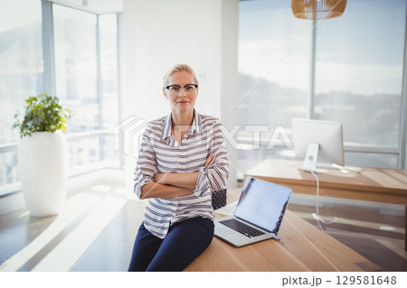 Mature woman working on open laptop at modern office near planter and monitor in business attire 129581648