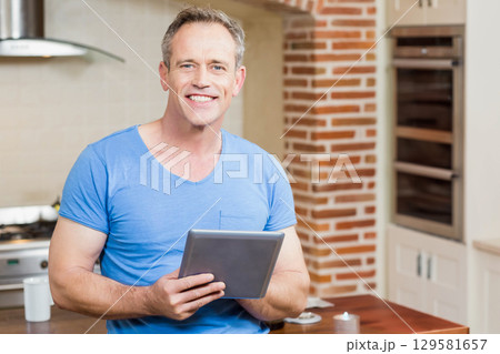 Senior man holding tablet computer and smiling in modern kitchen at home with gas stovetop Senior man holding tablet computer and smiling in modern kitchen at home with gas stovetop 129581657