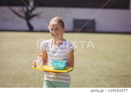 Female child holding yellow plastic tray with bottle, turquoise bowl and spoon on grassy lawn Female child holding yellow plastic tray with bottle, turquoise bowl and spoon on grassy lawn 129581677