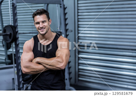 Muscular man wearing black tank top standing at gym by squat rack with plates, copy space Muscular man wearing black tank top standing at gym by squat rack with plates, copy space 129581679