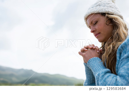 Woman standing in field closing eyes wearing light blue sweater and white beanie, copy space 129581684