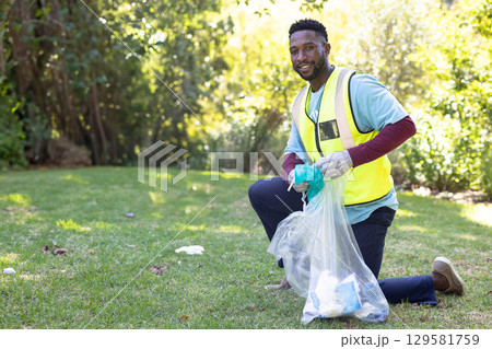African American man in safety vest kneeling in park collecting litter into trash bag, copy space African American man in safety vest kneeling in park collecting litter into trash bag, copy space 129581759