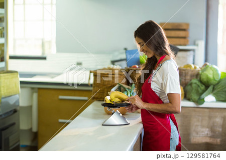 Woman weighing bananas on digital scale at produce counter with wicker baskets, copy space Woman weighing bananas on digital scale at produce counter with wicker baskets, copy space 129581764