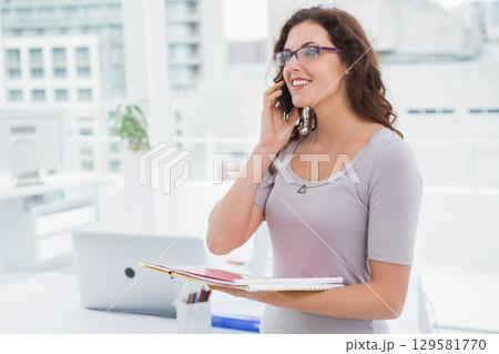 Woman holding notebooks and using smartphone at desk with closed laptop, pen holder, copy space 129581770