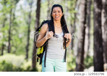 Asian woman wearing hiking attire standing on pine trail holding black and yellow hiking backpack Asian woman wearing hiking attire standing on pine trail holding black and yellow hiking backpack 129581796