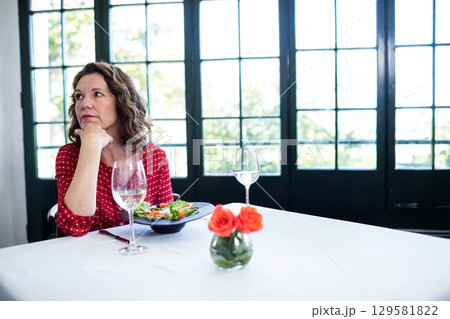 Woman wearing red blouse leaning chin on hand gazing at restaurant with salad bowl, copy space Woman wearing red blouse leaning chin on hand gazing at restaurant with salad bowl, copy space 129581822