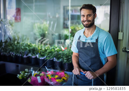 Man wearing apron arranging bouquets on wheeled cart in flower shop with glass panels, copy space 129581835