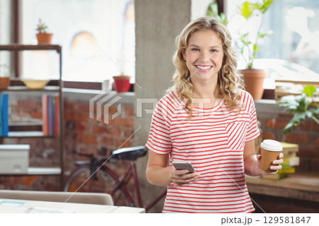 Teenage girl standing in loft-style workspace holding smartphone and paper coffee cup, copy space Teenage girl standing in loft-style workspace holding smartphone and paper coffee cup, copy space 129581847