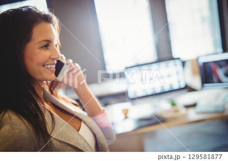 Woman in light-colored blazer talking on smartphone beside desk in office workspace, copy space 129581877