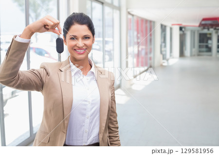 Female sales representative standing in dealer showroom smiling and holding car key fob, copy space Female sales representative standing in dealer showroom smiling and holding car key fob, copy space 129581956