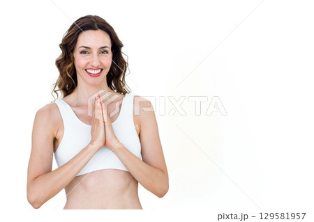 Woman smiling and holding palms together in prayer pose in studio wearing white sports bra Woman smiling and holding palms together in prayer pose in studio wearing white sports bra 129581957