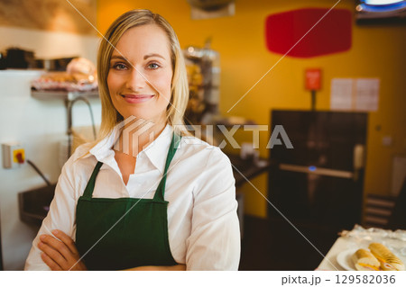 Female bakery staff wearing green apron displaying croissants and bread baskets at bakery counter Female bakery staff wearing green apron displaying croissants and bread baskets at bakery counter 129582036