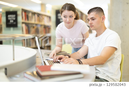 Girl and boy studying for exam together in library - using books and laptop Girl and boy studying for exam together in library - using books and laptop 129582043