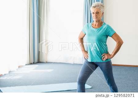 Senior woman in sportswear holding wide-legged pose on yoga mat in yoga studio, copy space 129582071