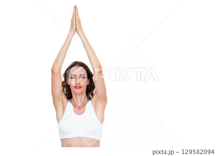 Woman raising arms above head while holding palms together and wearing sports bra in studio Woman raising arms above head while holding palms together and wearing sports bra in studio 129582094