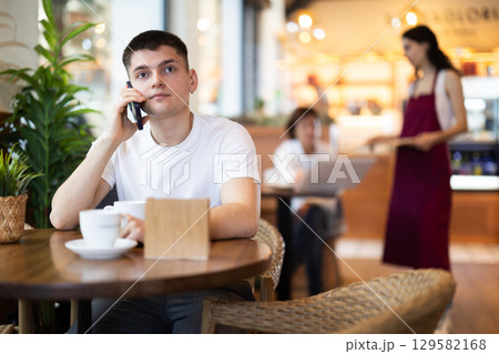 Young man talking on phone in cafe Young man talking on phone in cafe 129582168