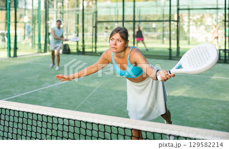 Woman playing padel tennis match during training on court Woman playing padel tennis match during training on court 129582214