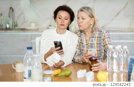 Adult daughter and elderly mother scan barcode on food package together using smartphone 129582245