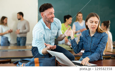 Dissatisfied female student showing stop gesture to annoying male friend at auditorium of university during break between lectures 129582358