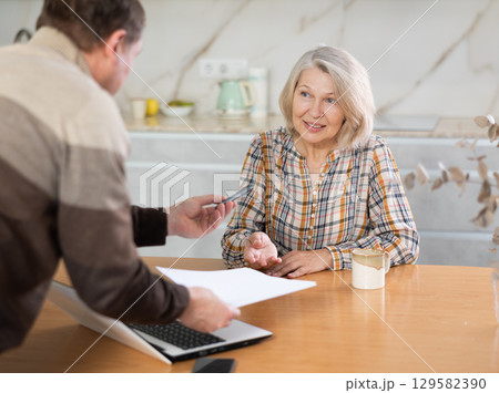 Male financial agent tells an elderly woman terms of microloan. Offers to sign documents Male financial agent tells an elderly woman terms of microloan. Offers to sign documents 129582390
